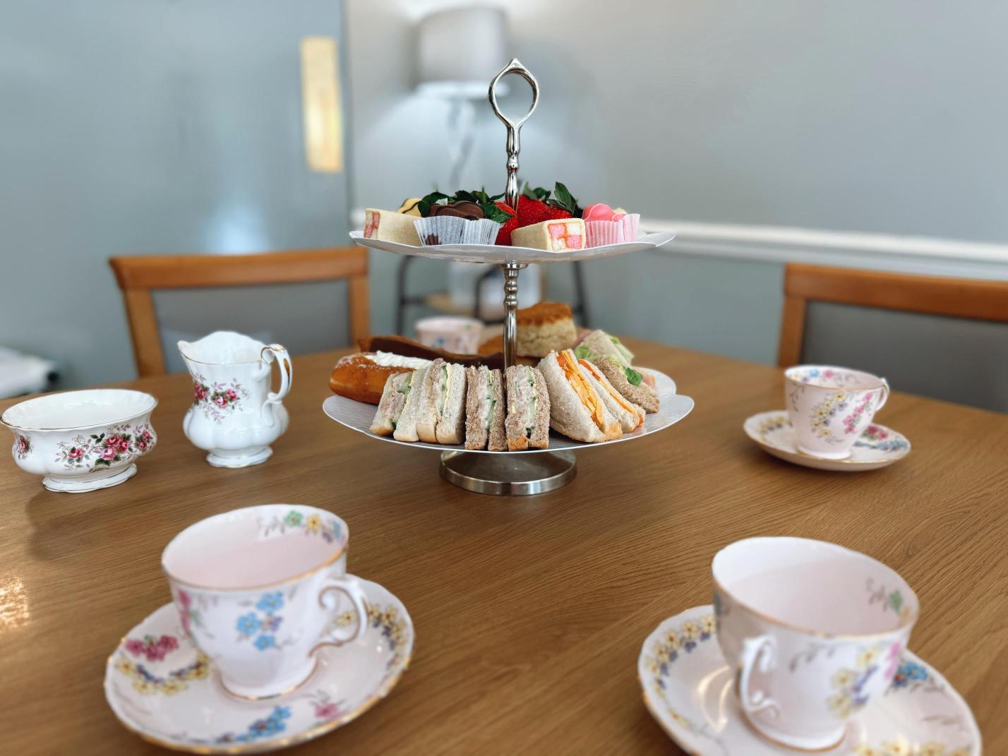 Selection of sandwiches and cakes for afternoon tea with lots of tea cups.