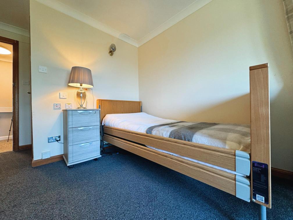 Wooden single bed with grey checkered sheets in a cozy room.