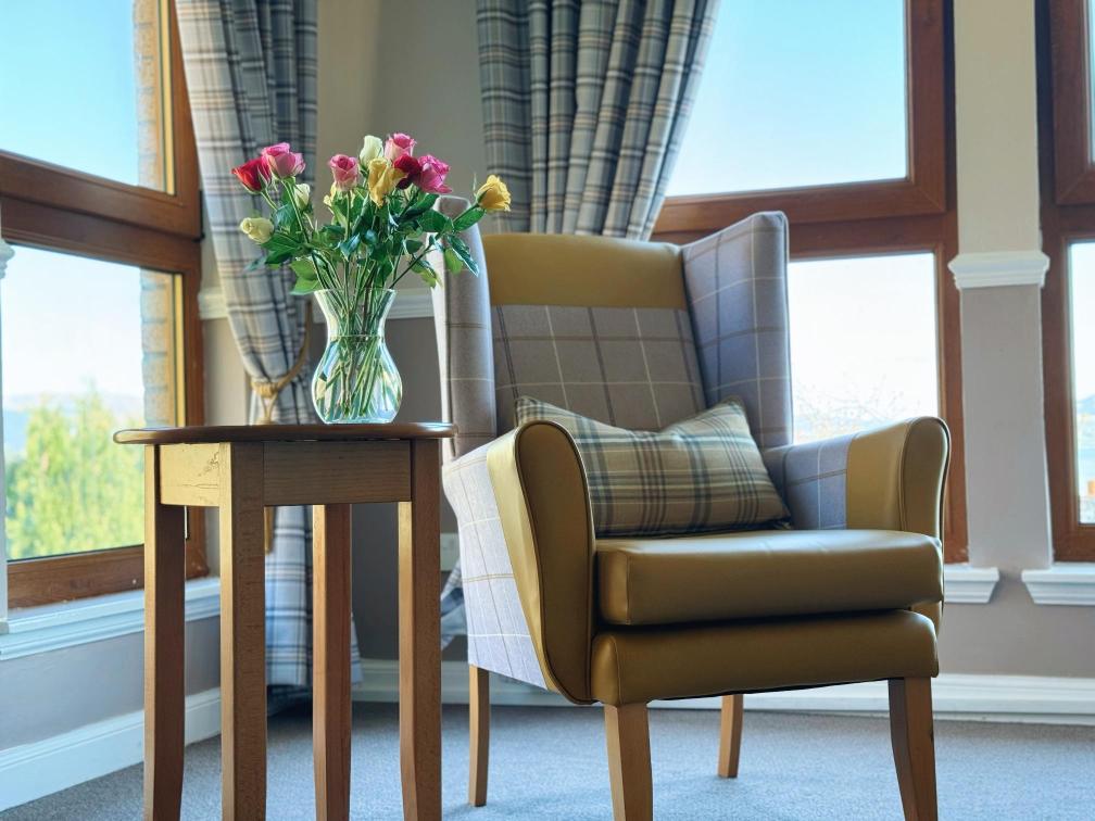 Selection of bright flowers in a vase next to an armchair.