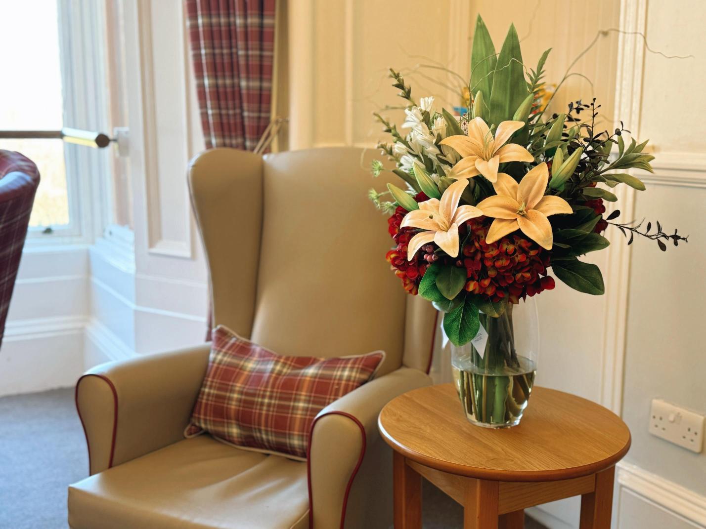 Selection of beautiful autumnal flowers in a vase next to an armchair.