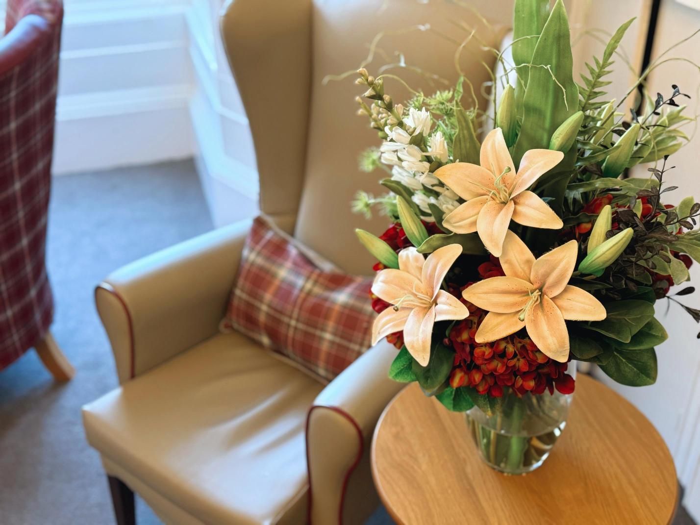 Selection of beautiful lilies in a vase next to an armchair.