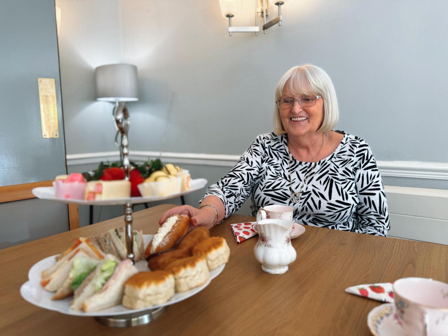 Selection of sandwiches and cakes for afternoon tea with a lady smiling.