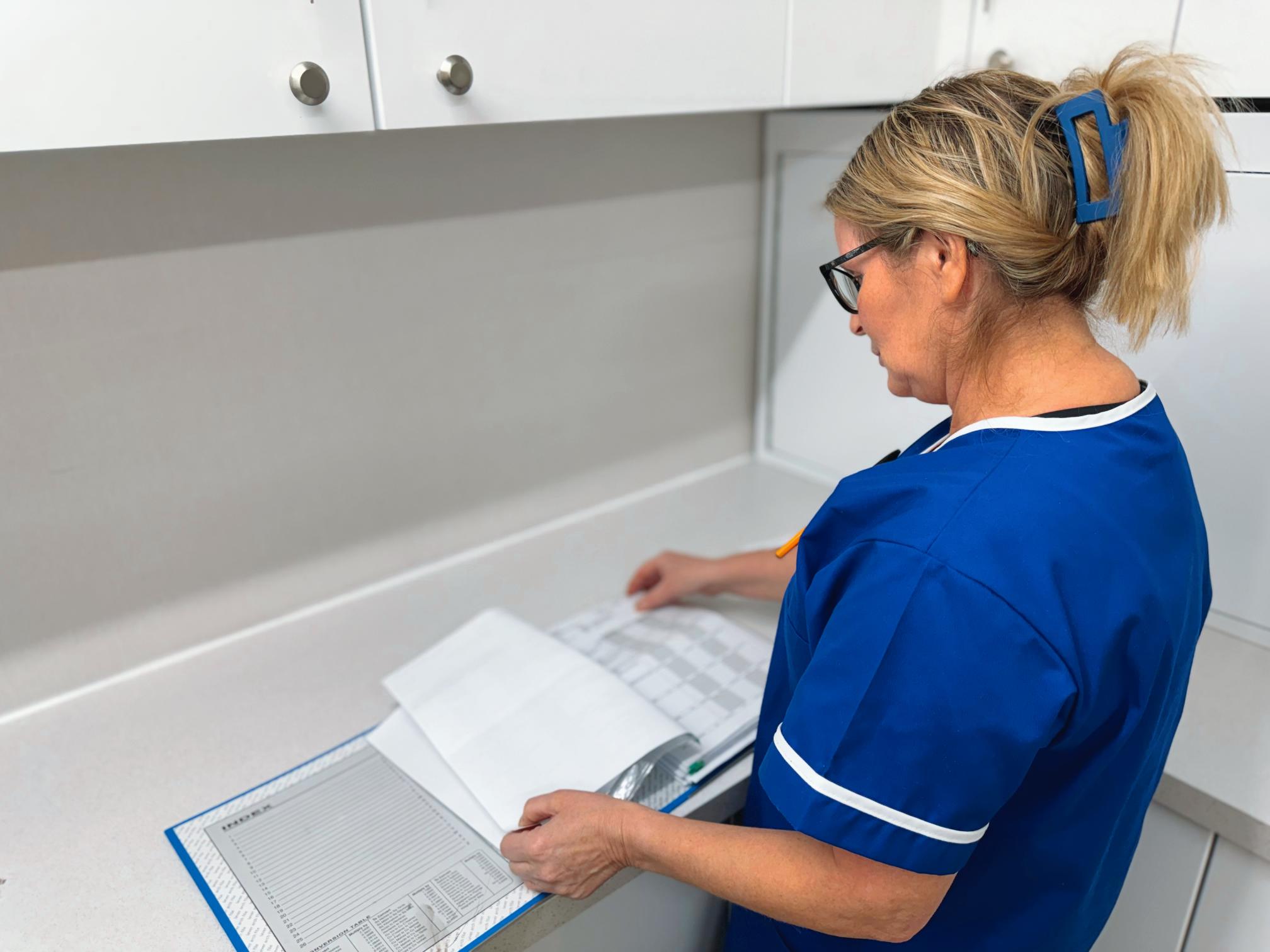 Healthcare nurse in a blue uniform checking patient notes.