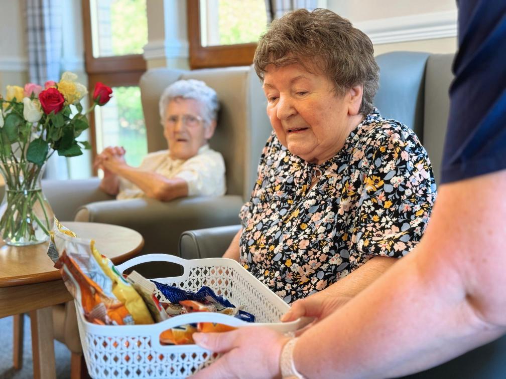 Resident of the care home choosing from a basket of snacks.