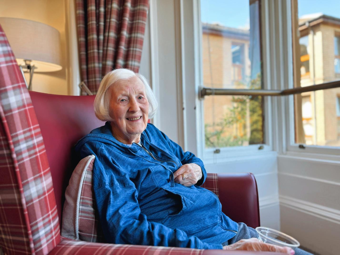 Care home resident sitting in an comfy red armchair.