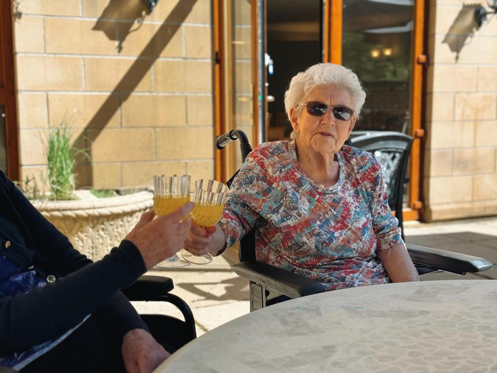 Care home resident enjoying the sunshine with a glass of drink.