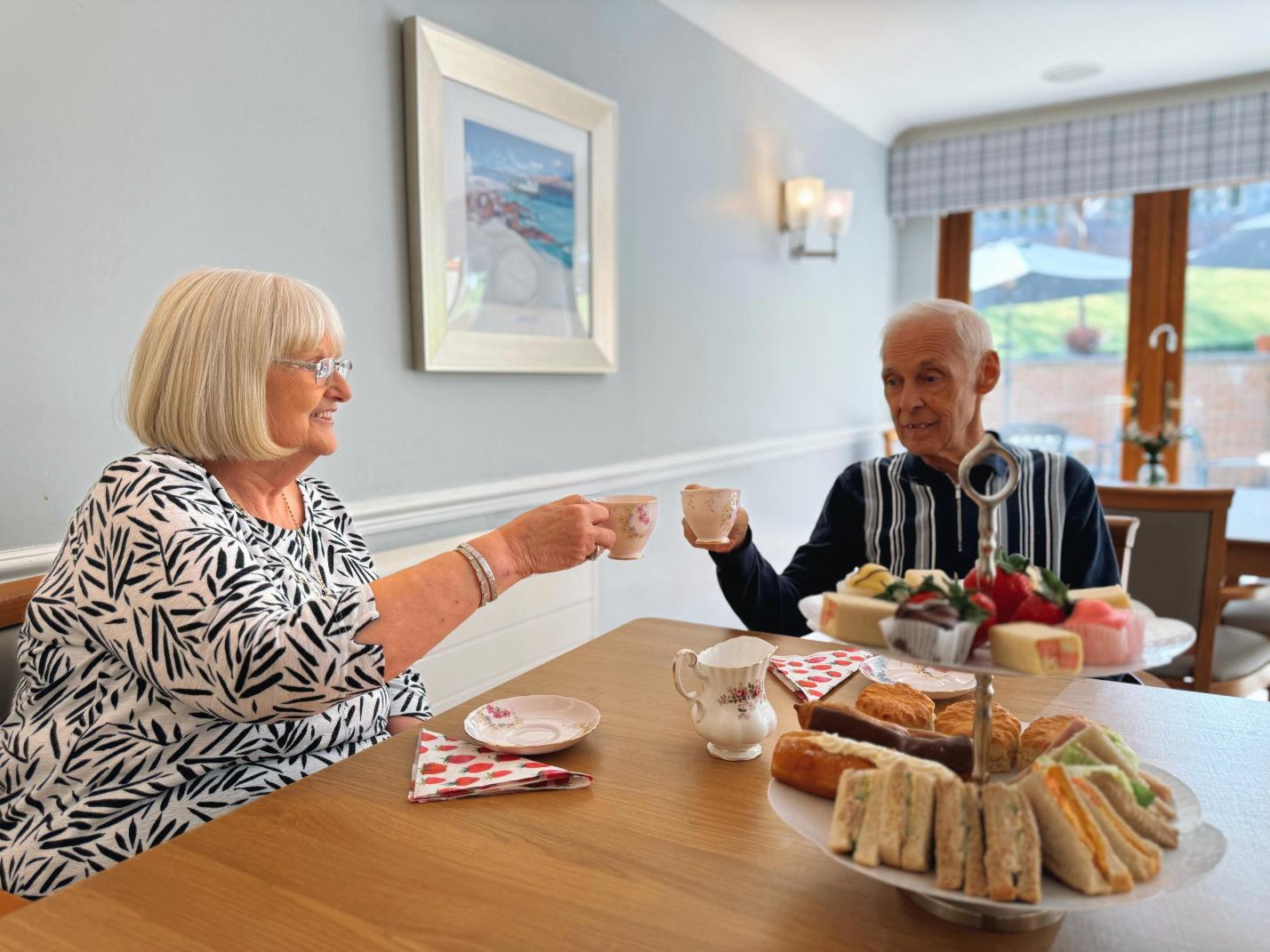 Two people with tea cups drinking tea at a wooden table.