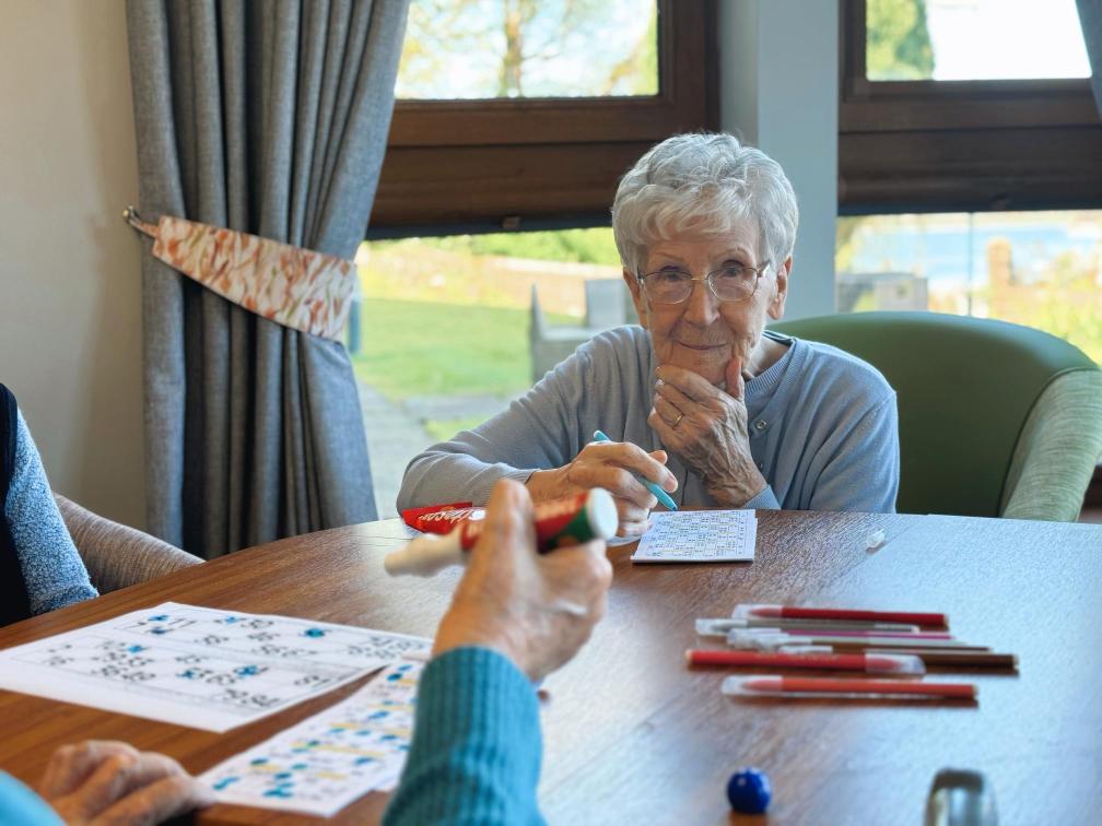 Care home residents playing bingo at a wooden table.