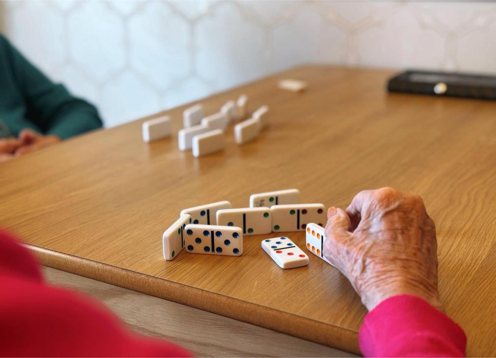 Closeup of two people playing dominoes at a wooden table.